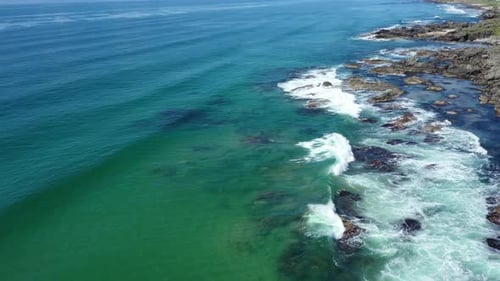 Aerial shot looking along the west coastline of Scotland, with a turquoise sea and waves crashing on