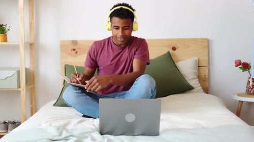 Man Studying on Bed with Laptop and Notebook