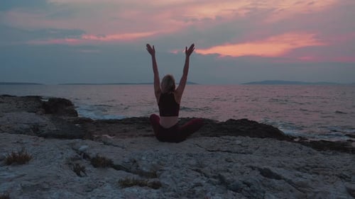 A beautiful shot of a woman sitting at the beach meditating and doing namaste pose at the sunrise.