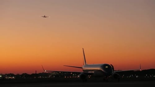 Airplane on runway at dusk with another jet silhouette in the sky
