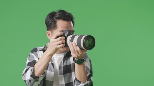Close Up Of Asian Photographer Using A Camera Taking Picture While Standing On Green Screen