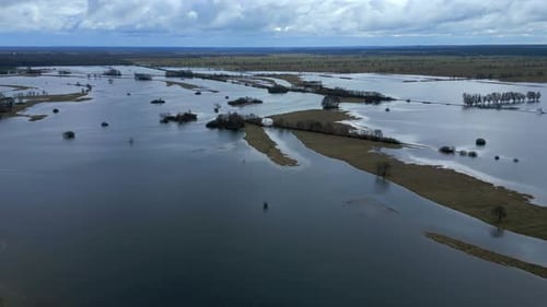 Aerial view of flooded landscape with submerged trees and fields under a cloudy sky