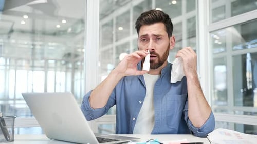 Sick businessman in suffering from cold and runny nose while sitting at a workplace in a business