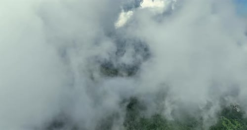Flying trough white fluffy clouds above green mountain peaks. Beautiful summer sunny day on the high