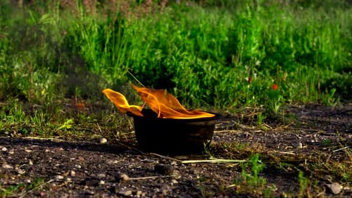 Bright Flames Blaze Through Aged Metal Canister Amid Lush Grass And Billowing Smoke Environment
