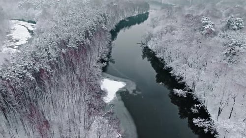 Aerial view of cold river and snowy forest in winter.