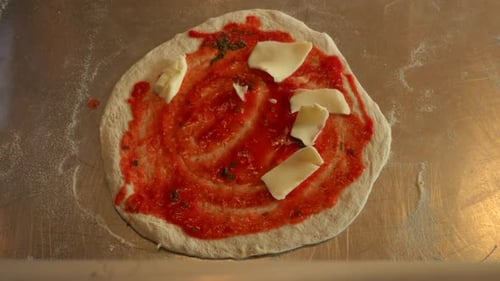 Top down shot of chef adding cheese to pizza, in a bright, medium close up shot