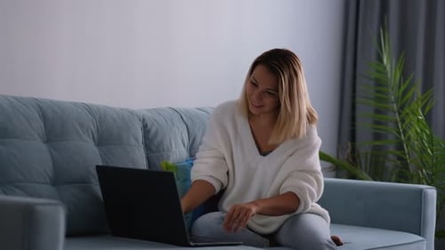 Woman Using Laptop Stretches on Couch at Home
