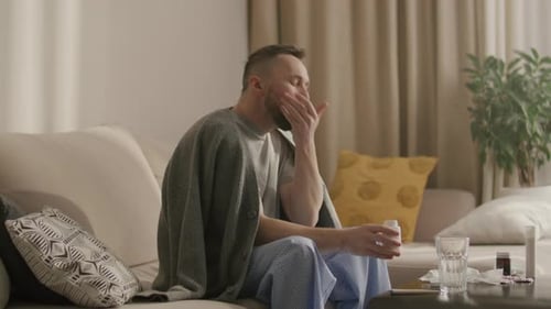 Man Takes Pills with Water Sitting on Couch