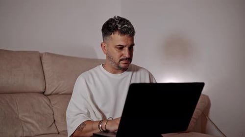 Man Using Laptop While Relaxing on Couch Indoors