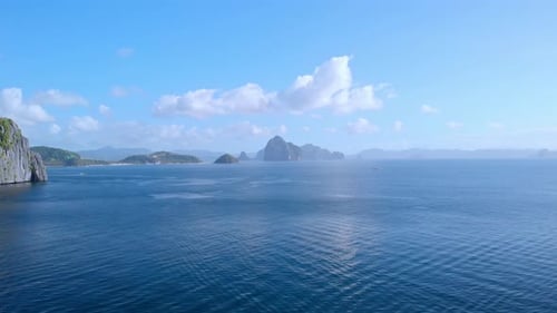 Forward flight over vast open sea toward scattered karst limestone islands rising from deep blue