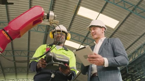 An engineer demonstrates robotic arm control to customer in industry factory.