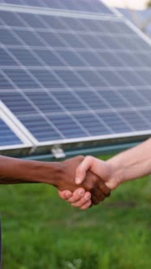 Handshake in Front of Solar Panels on Green Grass
