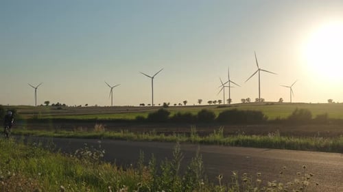 Cyclist riding on rural road with wind turbines at sunset