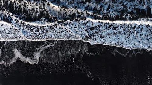 Aerial View of Black Sand Volcanic Beach with Crashing Waves Cinematic Long Drone Shot Serene and