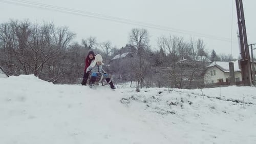 Kleiner Junge schiebt Bruder mit Winter-Schneeschlitten den Berg hinunter, Follow Pan