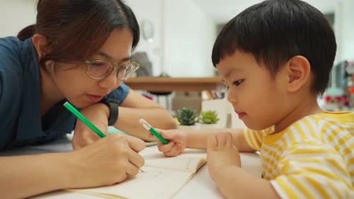Asiatische Mutter und kleiner Sohn zeichnen zusammen während der Homeschool-Kunstzeit zu Hause