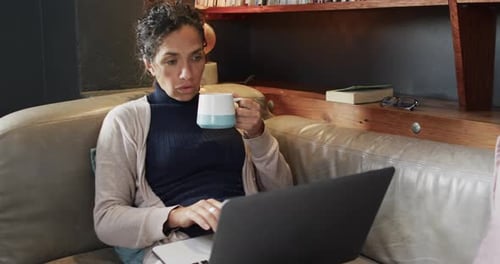 Woman Works on Laptop, Sips Mug on Couch