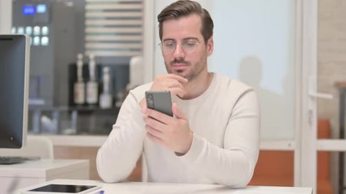 Young Man Browsing Internet on Phone in Office