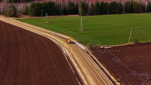 Grader ebnet einen Feldweg, der ein frisch bewirtschaftetes Feld von grünen Weiden trennt, Luftaufnahme