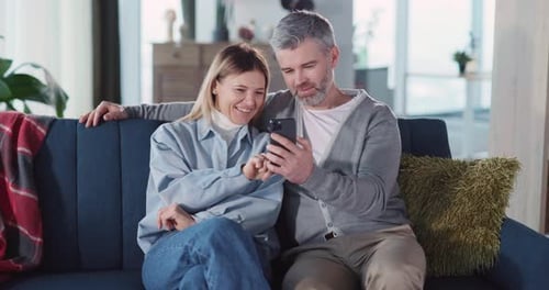 Couple Laughing Together Looking at Smartphone on Couch