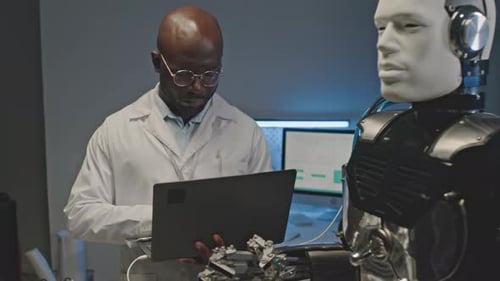 Black Male Engineer Using Laptop while Operating Human Robot