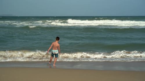 A Boy Stands and Looks at the Sea Waves on the Beach