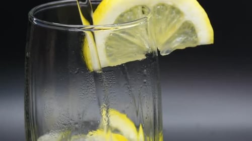 Pouring Mineral Water into a glass with lemon slices. Close-up shot.