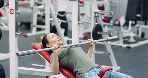 Footage of a Caucasian Woman Trains Chest Muscles Using Bench Press During Gym Workout