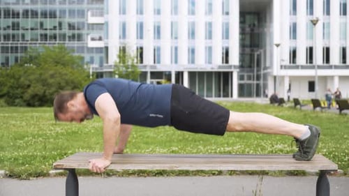 A Handsome Middleaged Caucasian Man Does Pushups on a Bench in a Park