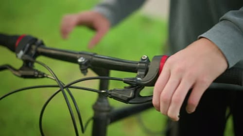 CloseUp of Hand Adjusting Bicycle Handlebar in Grassy Field