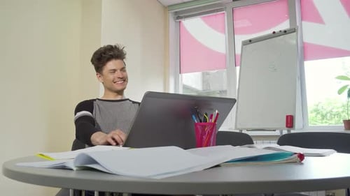 Cheerful Young Male College Student Engaged in Typing on His Laptop
