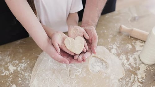 Hands of Family Holding Heart Shaped Cookie on Floured Countertop