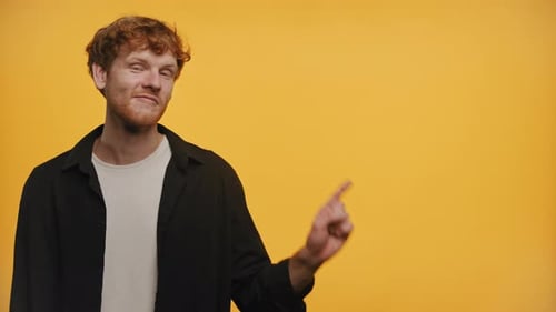 RedHaired Man Pointing at Copy Space and Smiling on Yellow