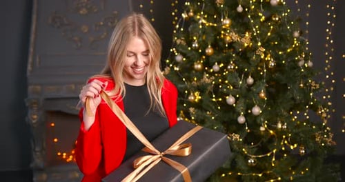 Woman Unwrapping Christmas Gift in Front of Tree