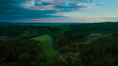 Curving Road Cutting Through Green Forest Under Dramatic Evening Sky Winding Asphalt Stretching