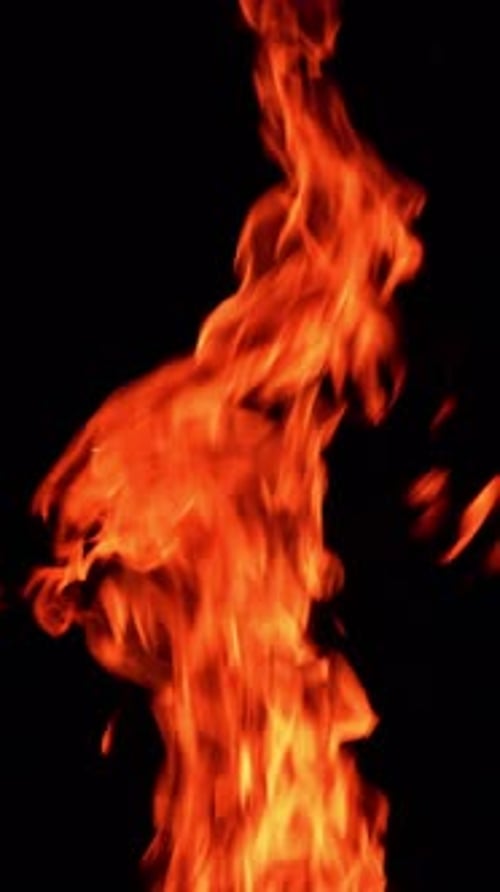 Thin narrow flame burning. Fire going up at the black backdrop. Orange spots flying up.