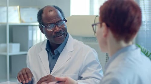 Senior General Practitioner Talking to Colleague at Meeting in Medical Office