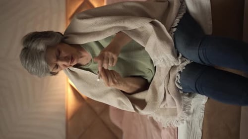 Senior Woman Checking Temperature with Thermometer in Bedroom