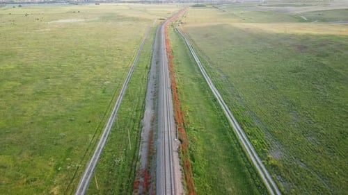 Luftaufnahme einer Eisenbahnstrecke, die durch ein üppiges Feld mit grünem Weizen auf dem Land führt