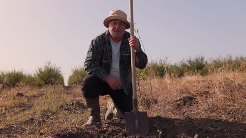 Farmer Kneeling With Newly Planted Tree in Field