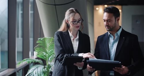 Corporate colleagues walking and discussing project while working on the go in modern office hallway