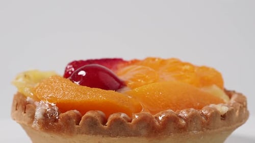 Pasteles giratorios con frutas sobre fondo blanco.