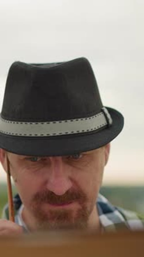 Focused Artist in Hat Concentrating on Task with Mosquitoes Around