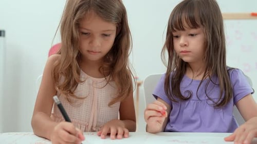 Two Young Girls Drawing Together at Table Indoors