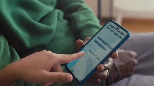 Hands of Multiethnic Couple Choosing Holiday Hotel on Smartphone