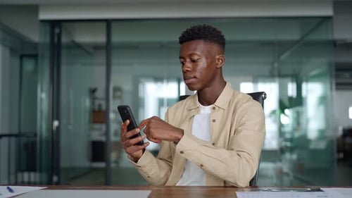 Smiling Busy African Business Man Sitting in Office Holding Cellphone
