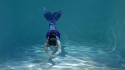 Positive schöne Meerjungfrau, die unter Wasser einen Kuss mit Wasserblasen sendet