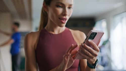 Smiling woman using phone in modern fitness setting