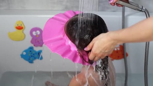 Mama wäscht einem kleinen Mädchen im Badezimmer das Shampoo vom Kopf. Mama badet das Baby
